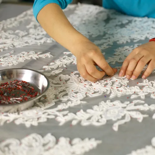 Artisan hand-beading intricate floral lace appliqué for a custom designer wedding gown.