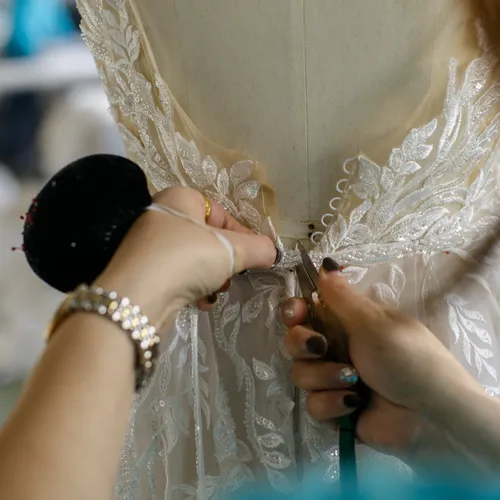 Detailed view of hands structuring the back of a couture wedding dress with lace and pearl buttons.
