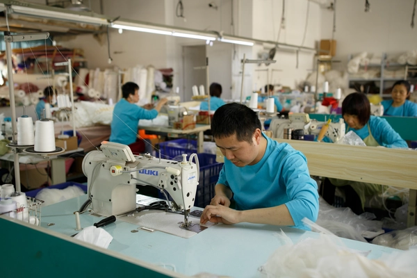 A professional artisan at the AiDo factory is focused on crafting a couture wedding gown at a sewing machine.
