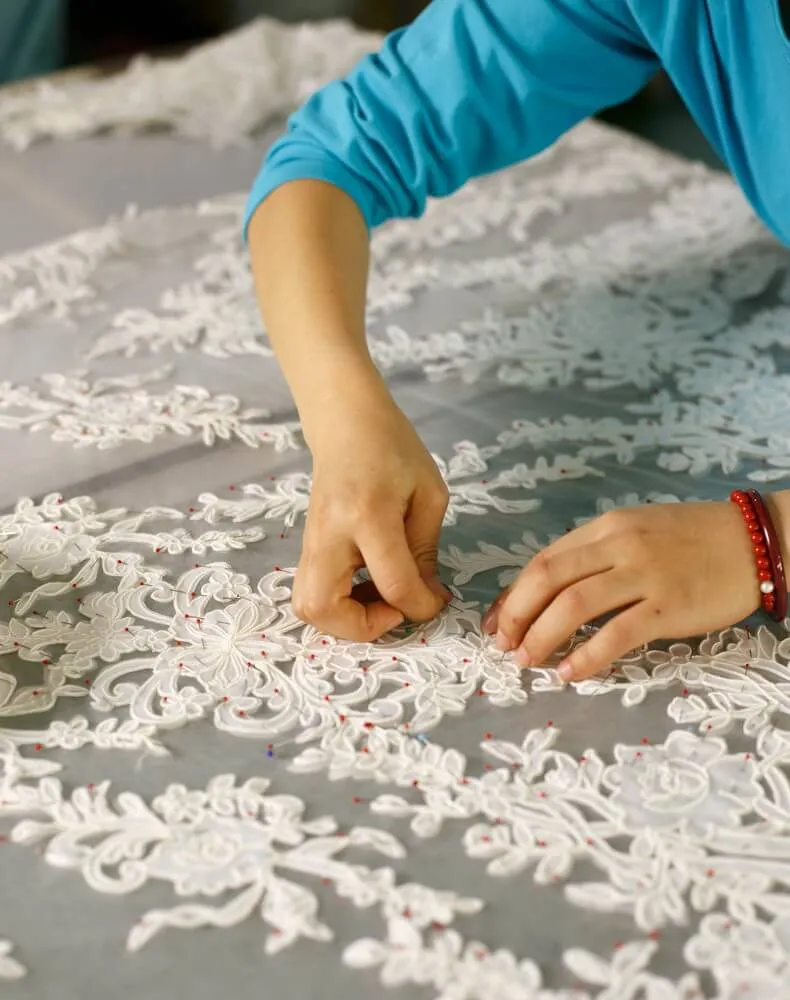 Contact AiDo for custom bridal manufacturing - close up of hand sewing lace details.