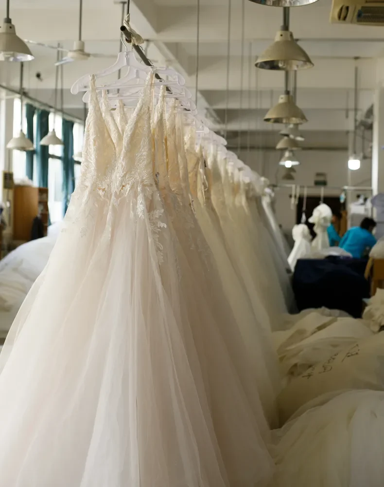 A rack of beautiful couture wedding dresses hanging in soft light, showcasing a variety of styles and design details available for wholesale to boutiques.
