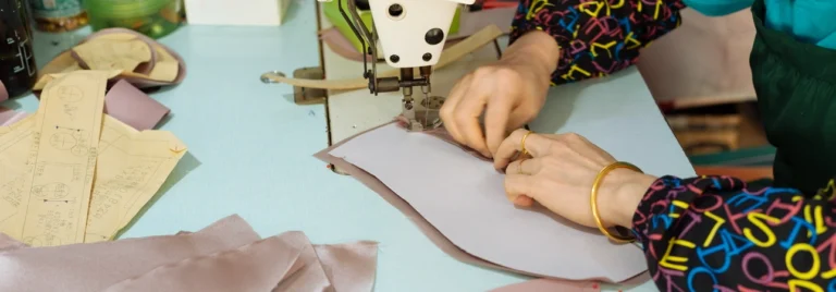 Primer plano de una costurera cosiendo intrincados detalles de tela en un vestido de novia, lo que representa nuestro compromiso con la artesanía de calidad. Contáctenos para consultas.