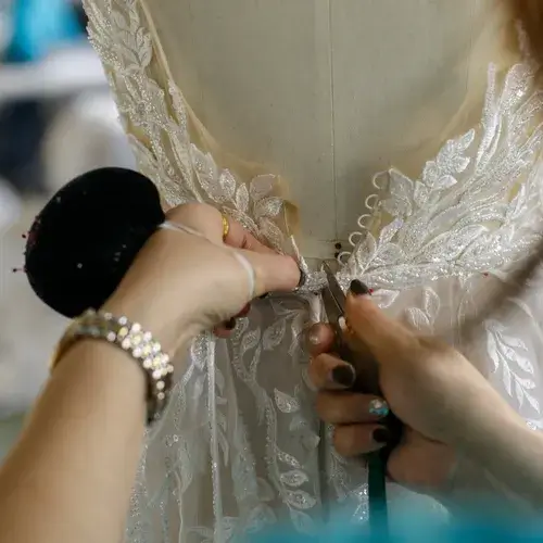 Detailed view of hands structuring the back of a couture wedding dress with lace and pearl buttons.